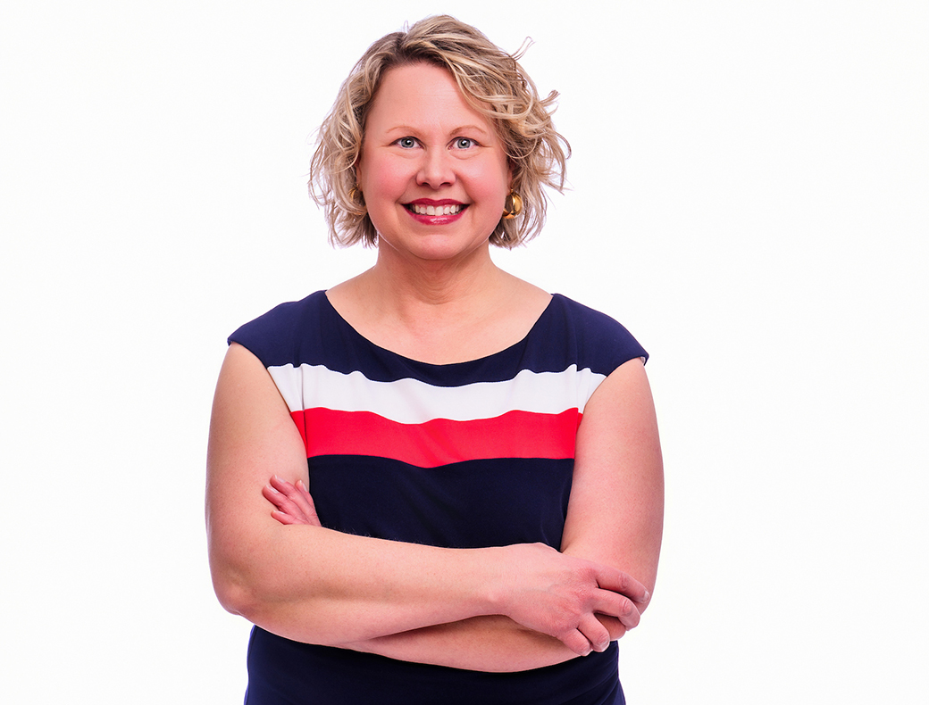 A photo of a woman, smiling with her arms crossed.