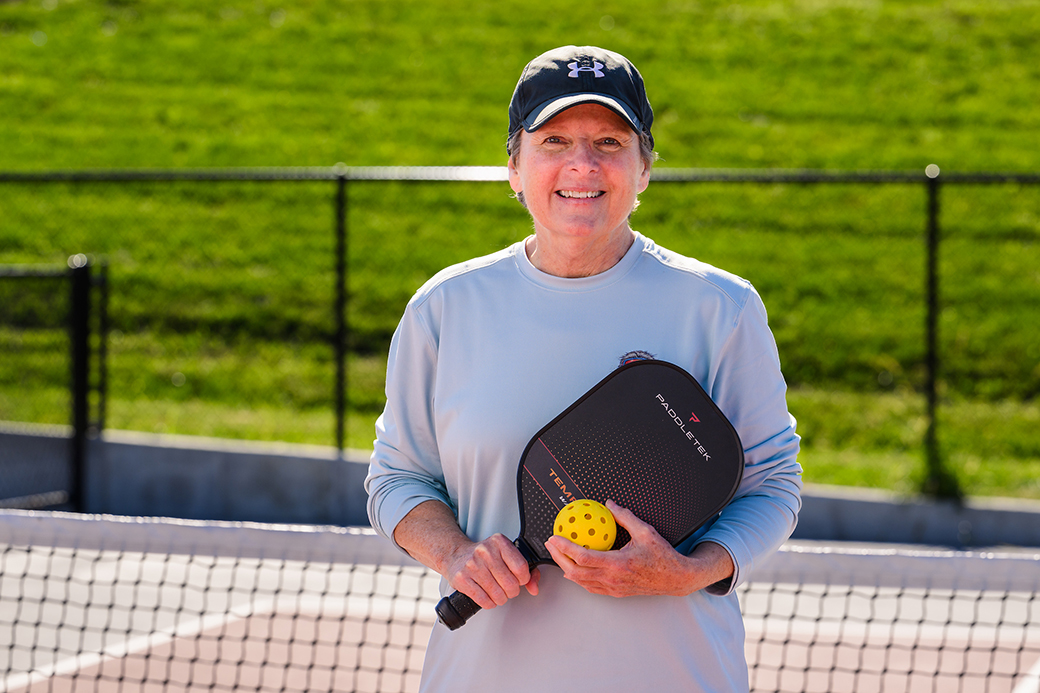 A woman smiling while holding a pickleball and paddle.