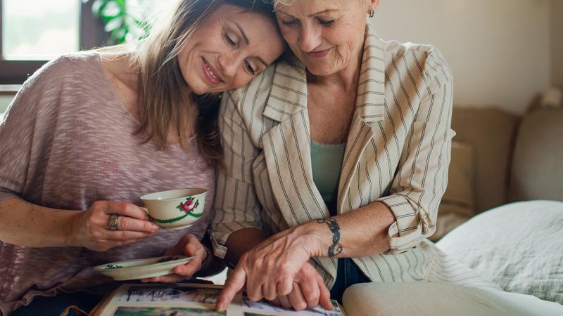 A mother and daughter sitting on a bed, smiling and hugging.