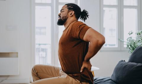 A man winces in pain as he touches his lower back.