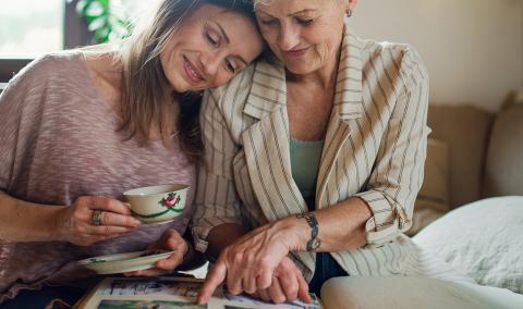 A mother and daughter sitting on a bed, smiling and hugging.